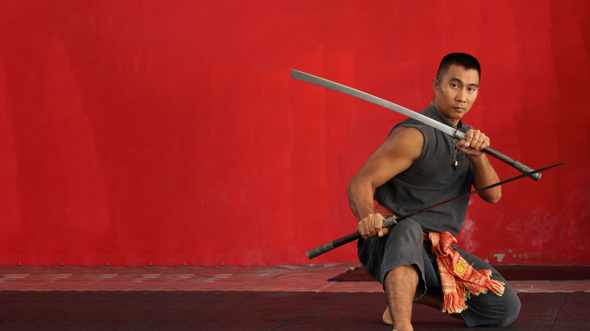 Krabi Krabong instructor holding a Thai sword against a red wall