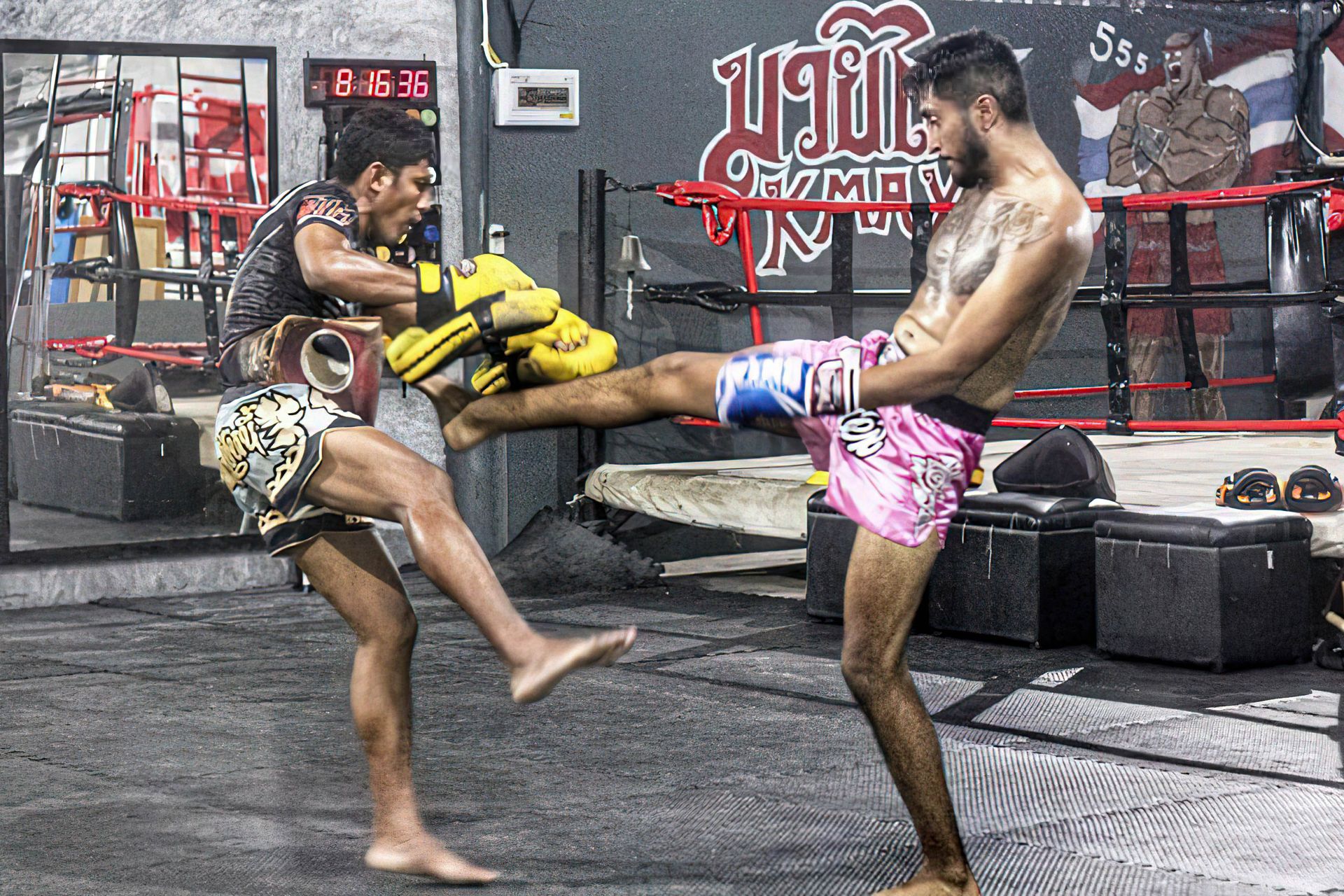 Student kicking pads held by a Thai trainer